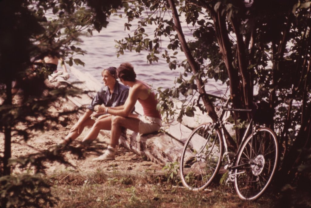 A young couple sitting on a log beside an Adirondack lake in 1973, a ten-speed bicycle leaning against the trees beside them