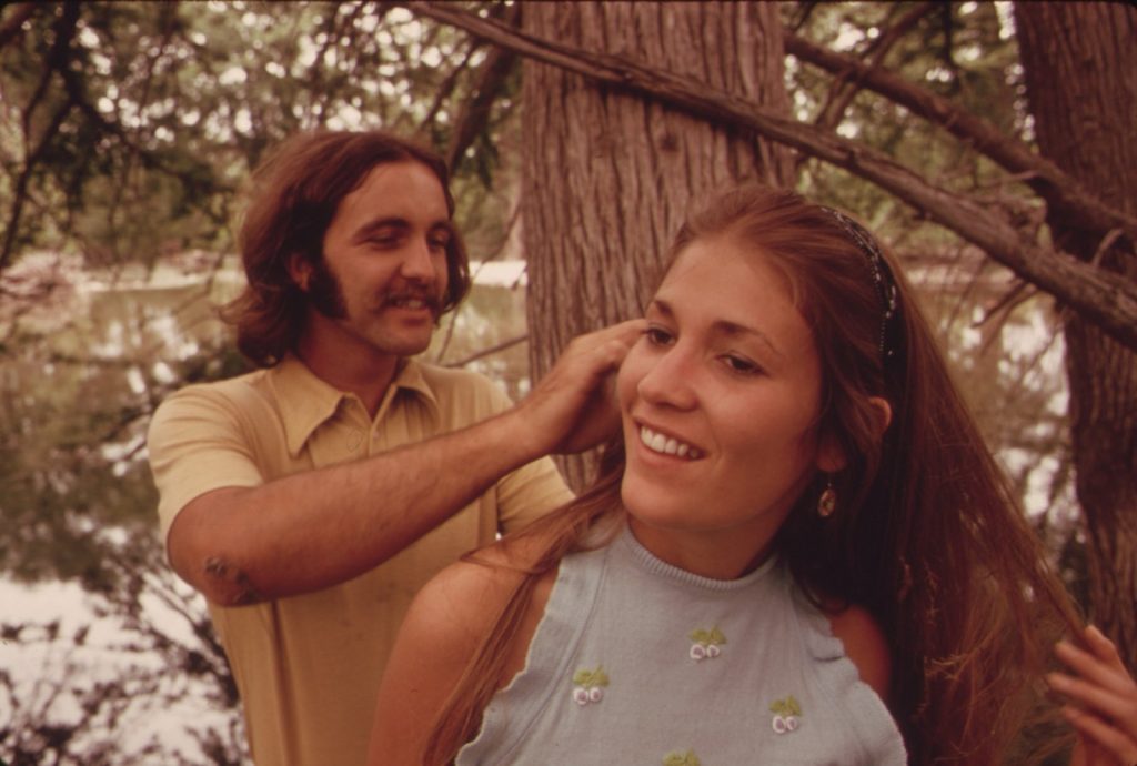 A young man smiling as he picks leaves out of a young woman’s long hair beside a Texas river in 1973