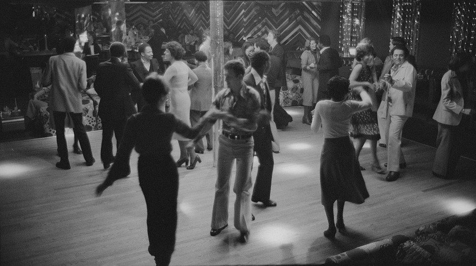 Couples dance on the lighted floor of The Plum, a Washington, D.C. discotheque, in October 1977, a young man in flared trousers mid-stride at the center