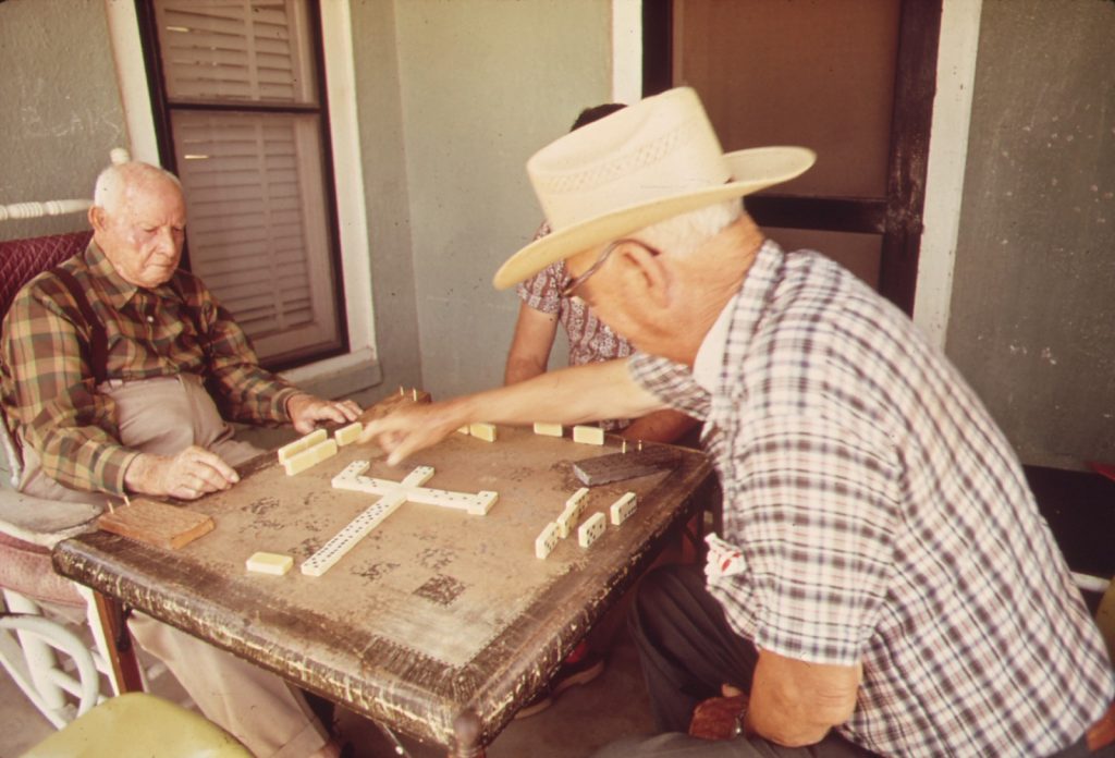 Two older men playing dominoes at a table on a porch