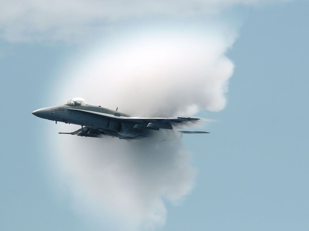An F A-18 Hornet in flight with a white condensation cloud around its shock waves