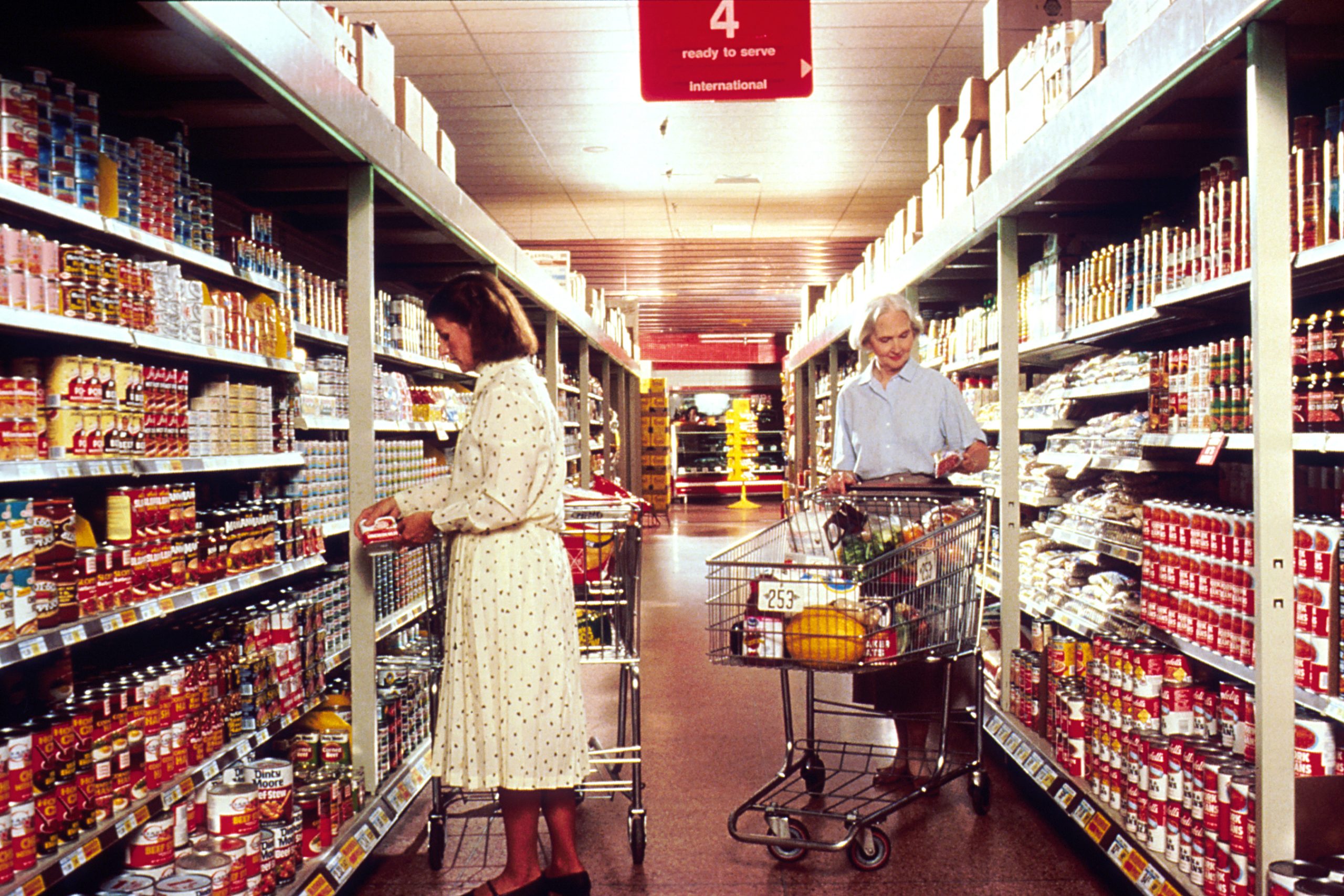 Two women with shopping carts selecting groceries in a supermarket aisle in March 1989