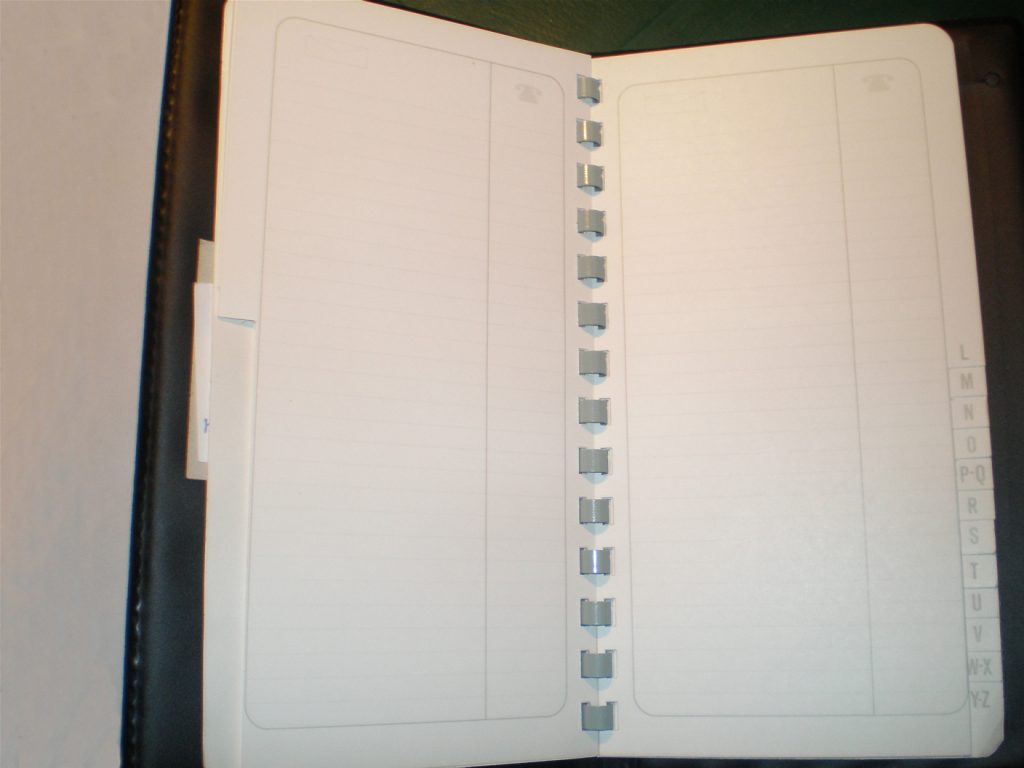 Open dark-covered address book with blank ruled pages, telephone symbols, and alphabet tabs