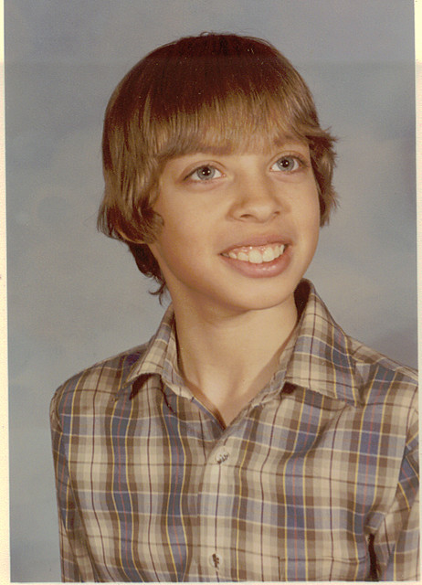 A school portrait of a smiling boy with straight brown hair and a plaid shirt against a blue-gray backdrop