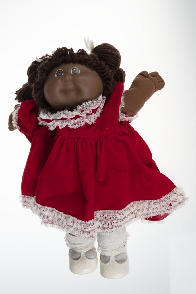 A 1984 Black Cabbage Patch Kid doll wearing a red velvet dress with white lace trim