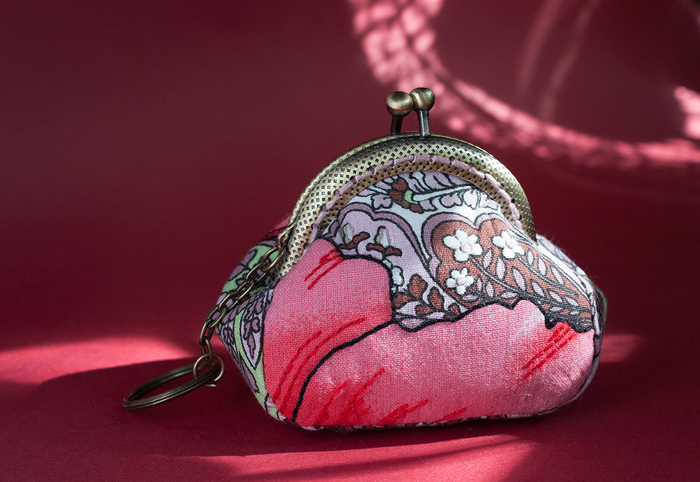Pink floral fabric coin purse with a metal kiss-lock clasp on red fabric