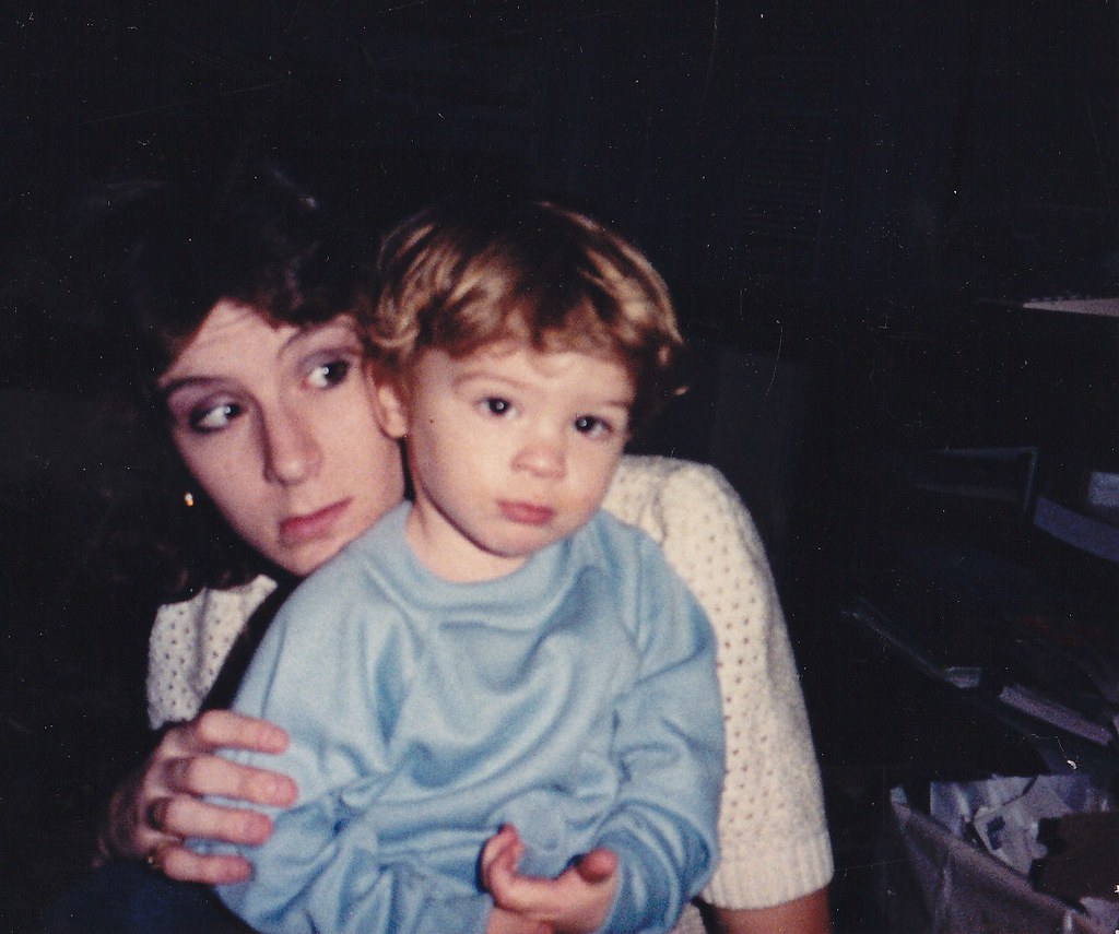 A dark-haired mother in a light knit top holds a toddler wearing pale blue pajamas