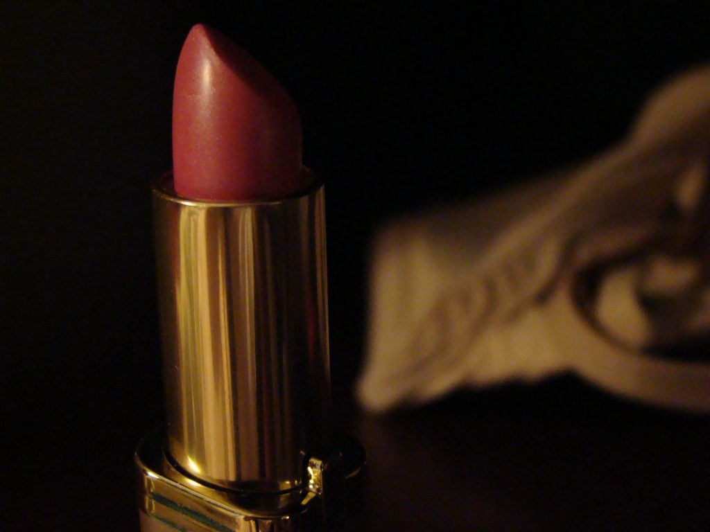 Pink-red lipstick extended from a gold-colored tube against a dark background