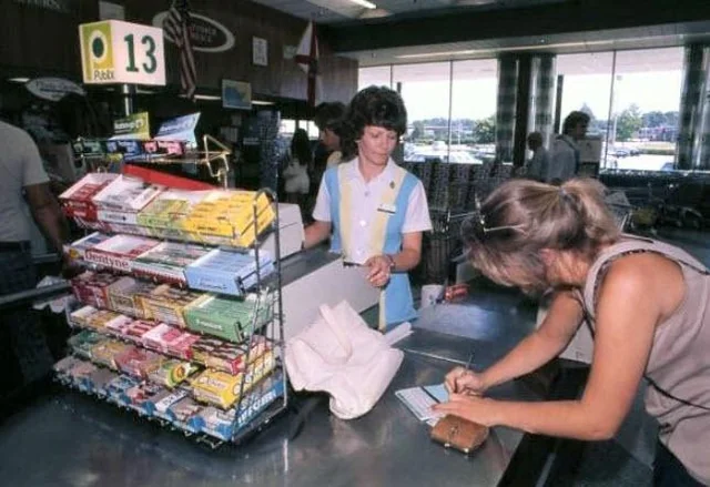 A woman writes a check at a Publix checkout while a cashier waits beside a display of gum and candy