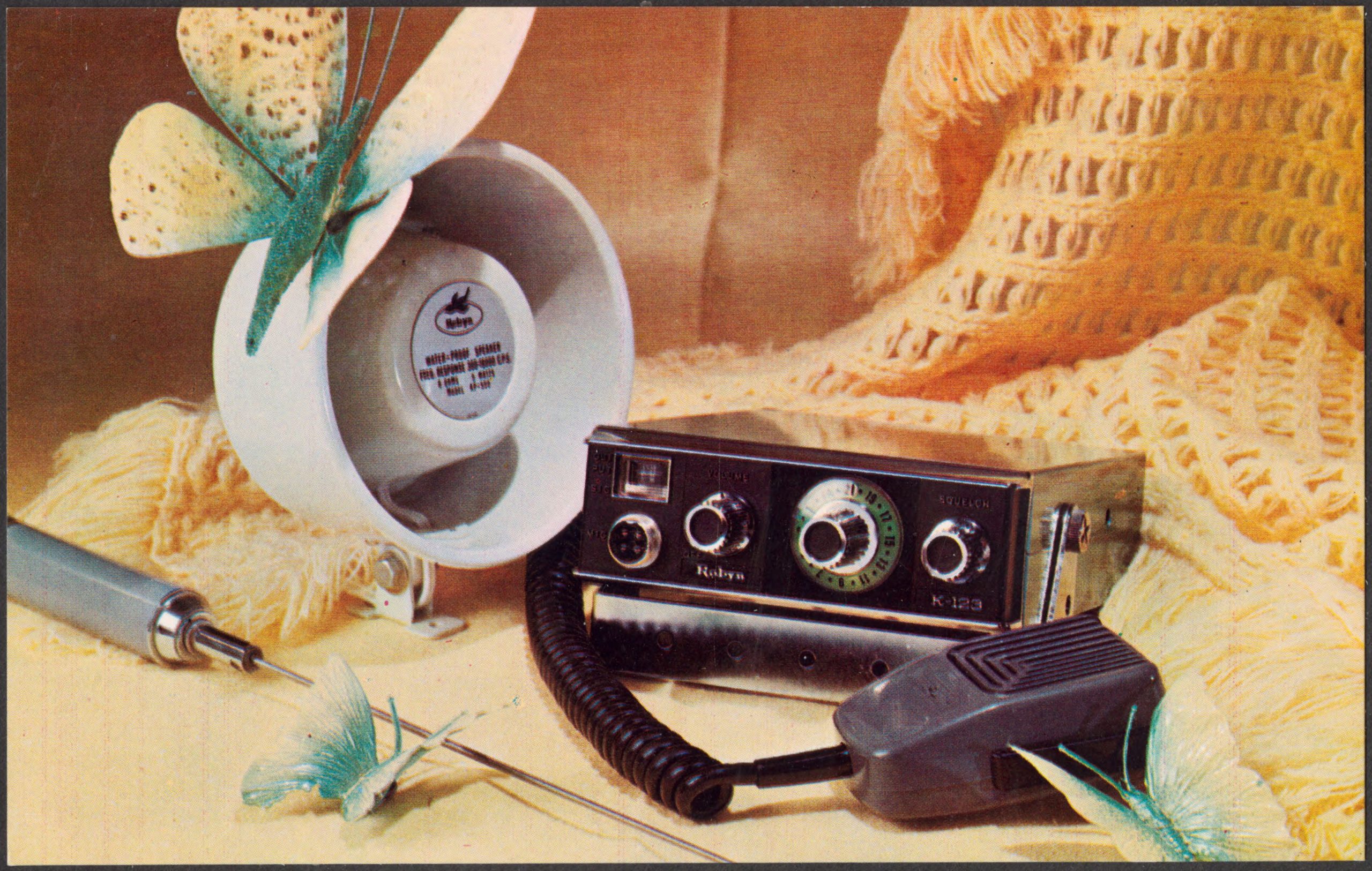 A Robyn K-123 CB radio with channel selector, control knobs, and a corded handheld microphone, beside a white external speaker.