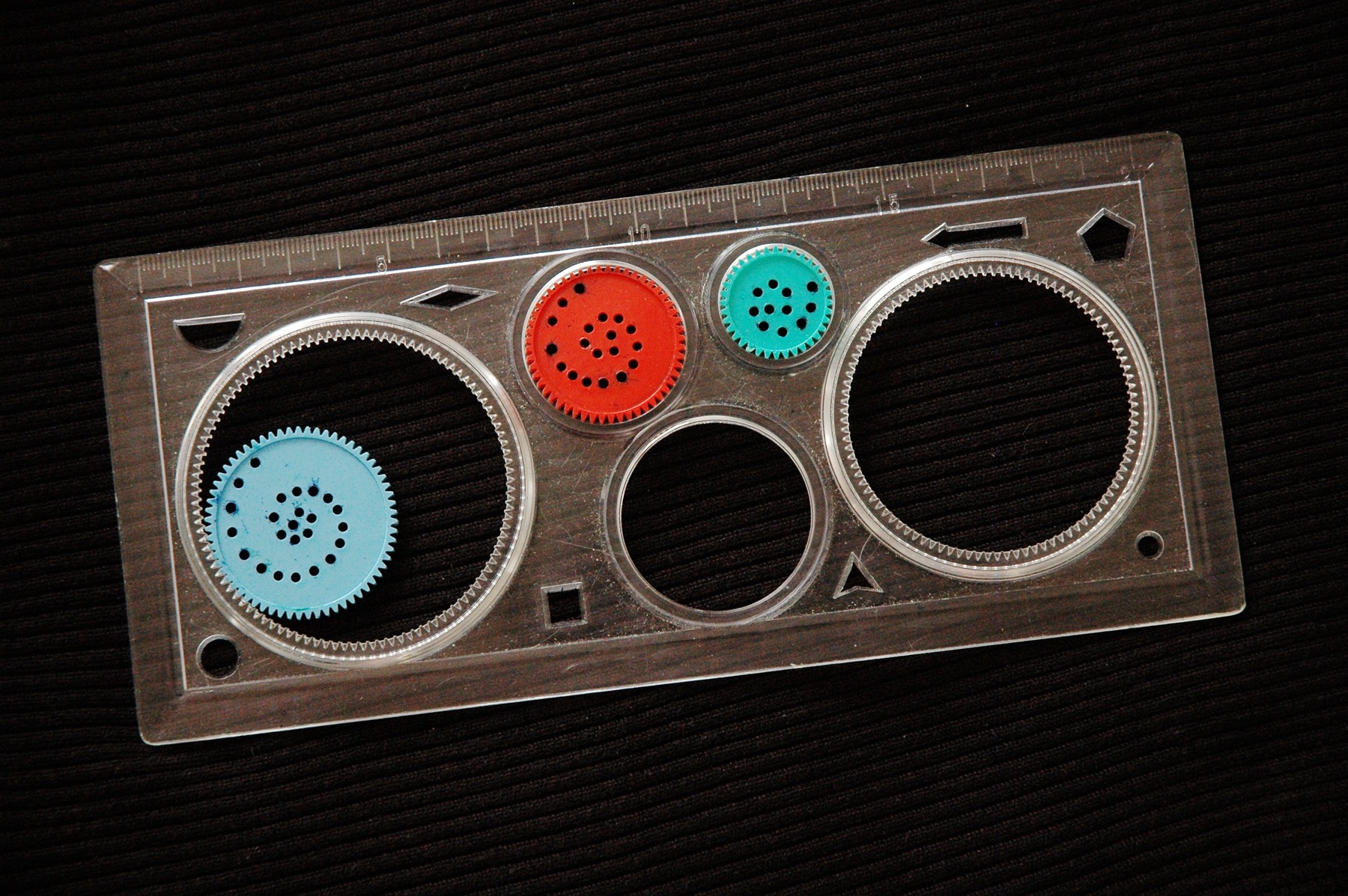 Clear plastic Spirograph rings and colored gears resting on dark fabric