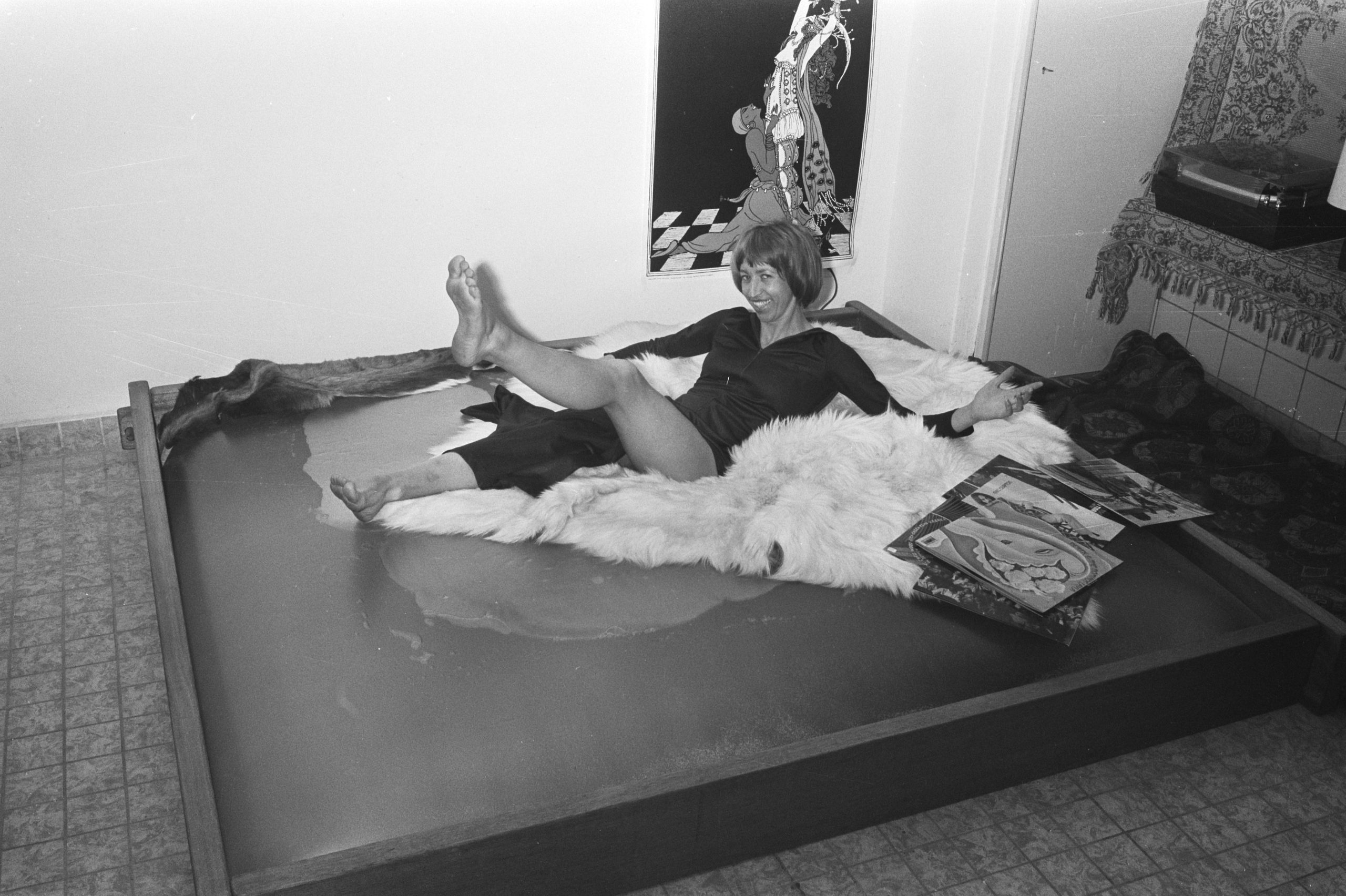 A woman reclines on a waterbed with a white fur covering during a demonstration.