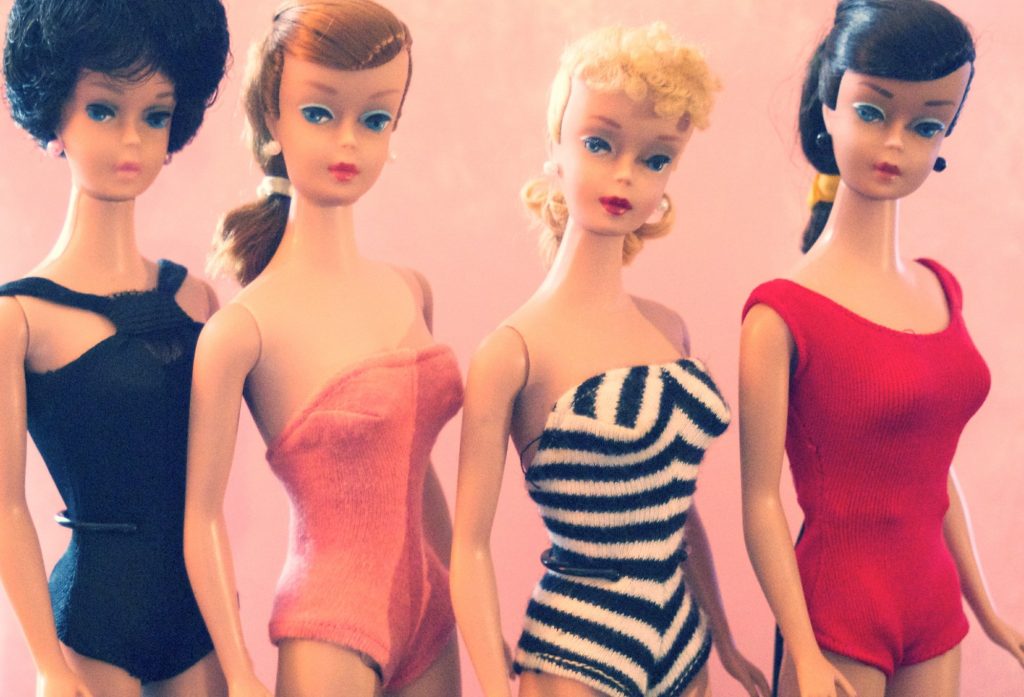 Four vintage Barbie dolls in swimsuits: a black-haired Bubblecut in black, a red-haired Swirl Ponytail in pink, a blonde No. 4 Ponytail in the black-and-white striped suit and a brunette Swirl Ponytail in red