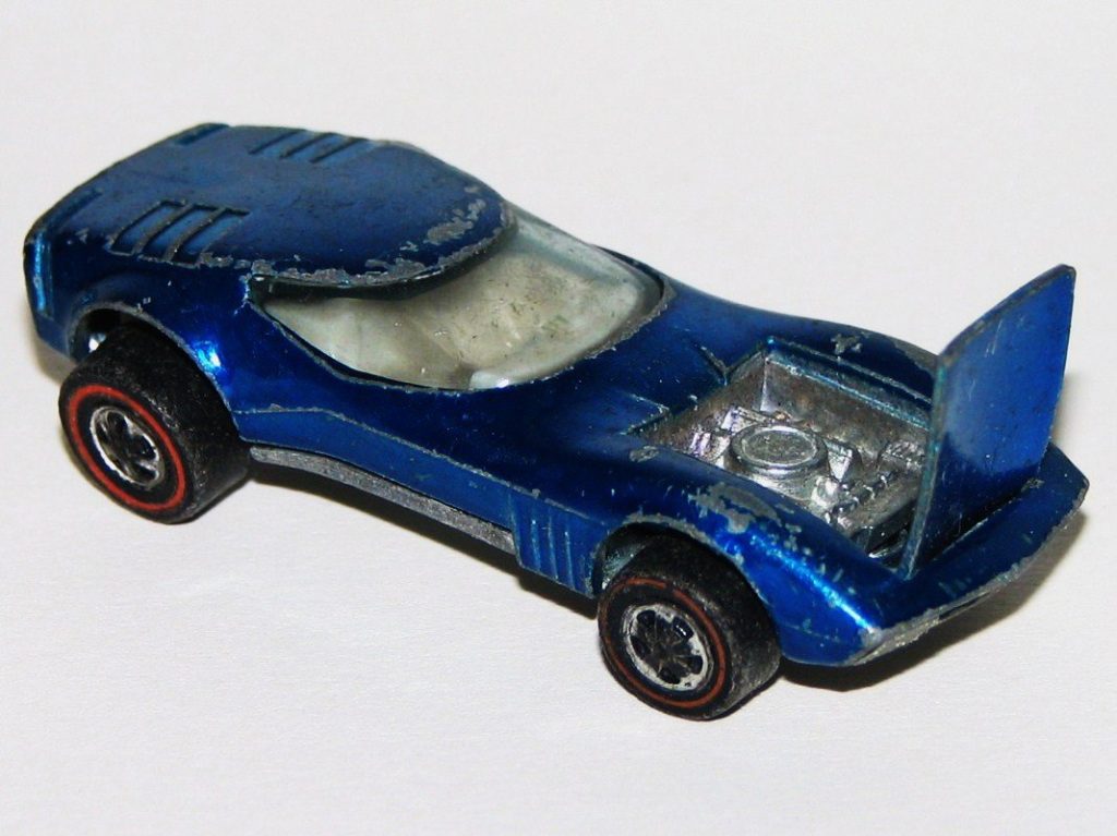 A blue Hot Wheels Torero die-cast car with chipped paint, its rear engine cover open, riding on wheels with thin red stripes on the tires