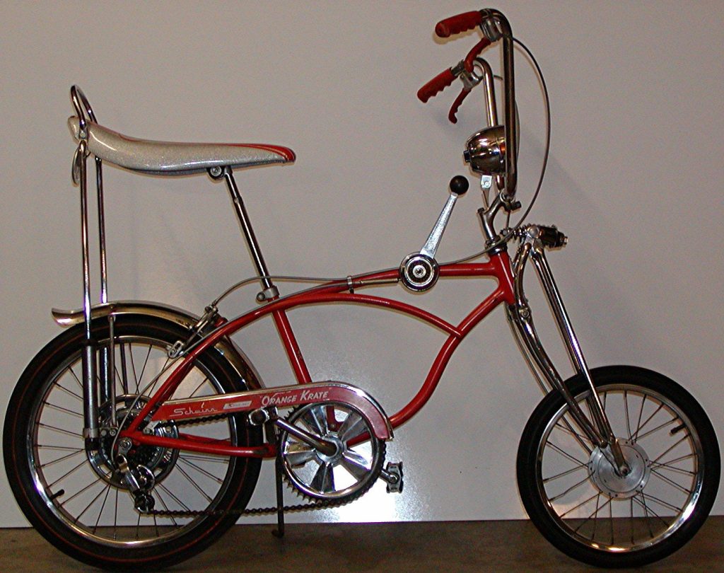 A 1968 Schwinn Orange Krate bicycle with a sparkly white banana seat, tall sissy bar, high-rise handlebars, a Stik-Shift lever on the top tube and a small front wheel on a springer fork