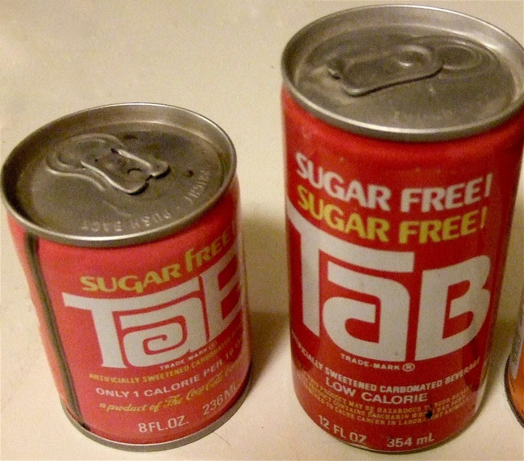 Two red TaB cans with pull-tab tops, an 8-ounce can and a 12-ounce can marked Sugar Free, with small print on the larger can warning that the product contains saccharin.