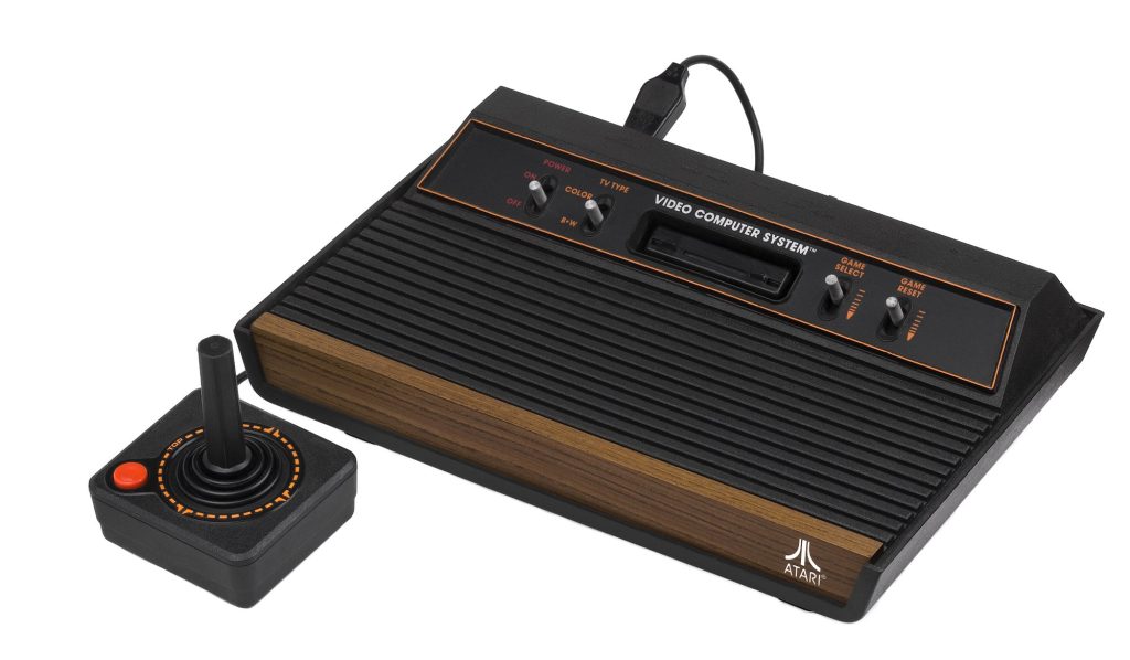 A black Atari 2600 Video Computer System console with a wood-grain front panel and four silver switches, beside a black joystick with a red button