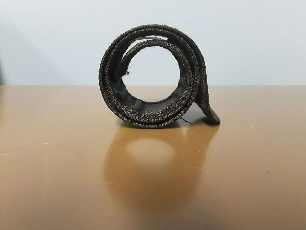 A fabric-covered slap bracelet curled into a coil, standing on a tan tabletop