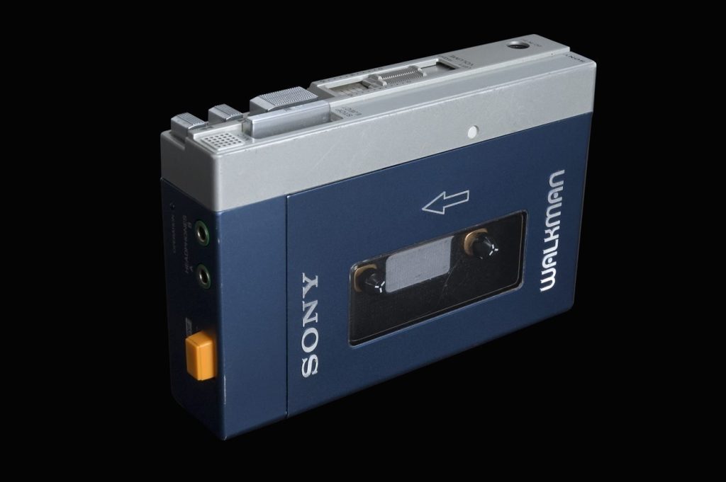 A blue and silver Sony Walkman cassette player with a window showing the tape, photographed on a black background