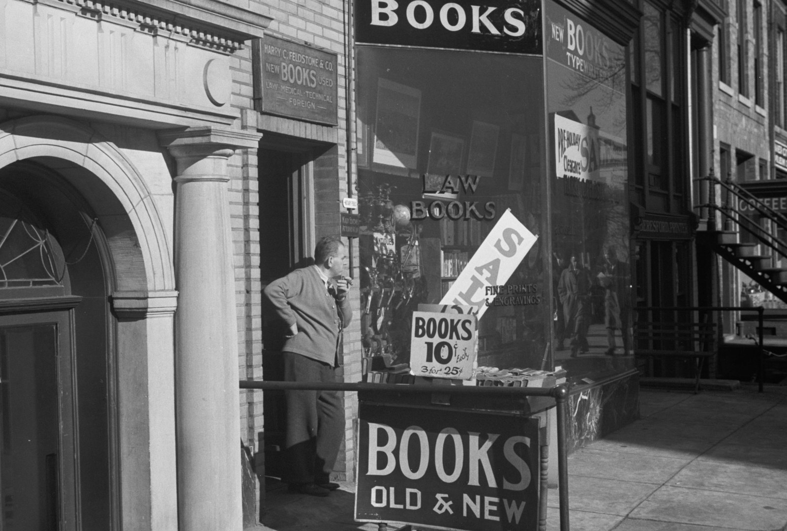 A man stands in the doorway of a bookstore with signs reading Books Old and New and Books 10 cents.