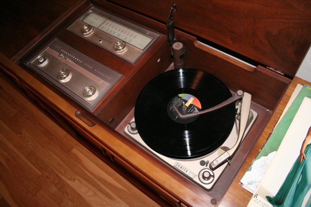 An LP sits on the automatic record changer of a wooden Zenith stereo console, beside the radio dials and a stack of album covers