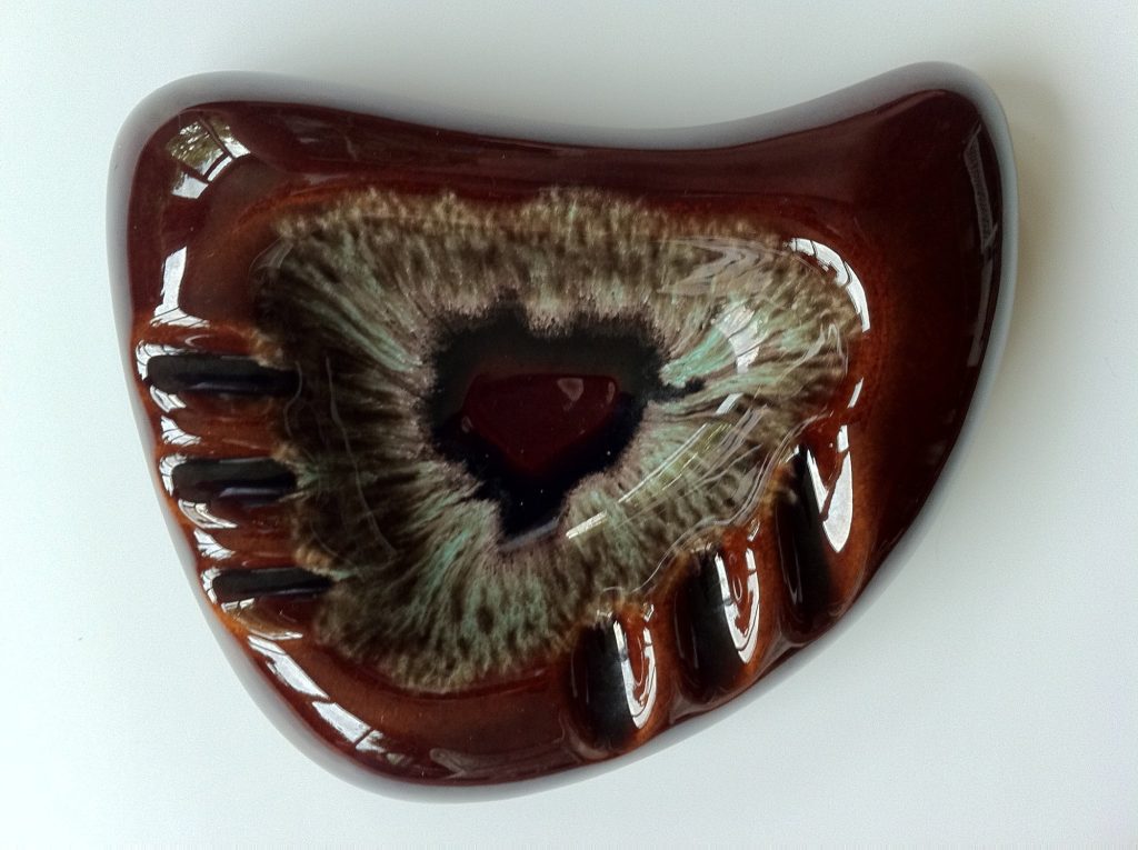 A glossy brown boomerang-shaped ceramic ashtray with a mottled green center and three cigarette rests