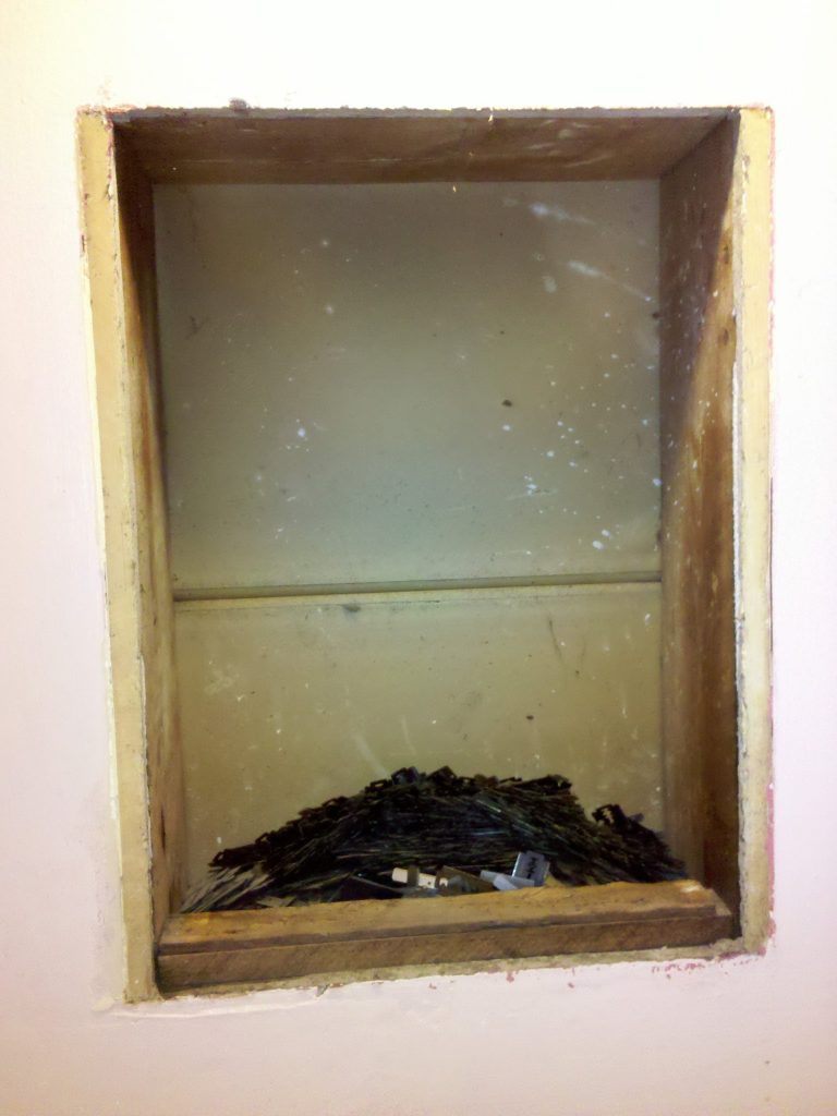 A heap of rusty used razor blades inside the wall cavity behind a removed medicine cabinet