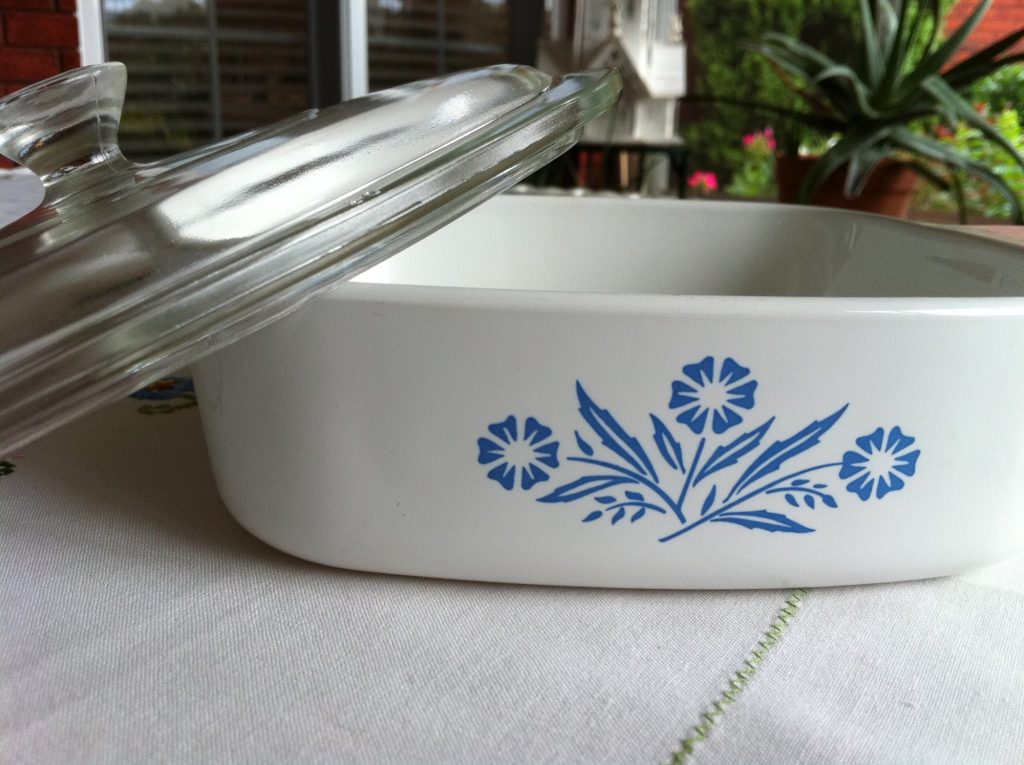 A white square casserole dish with a blue cornflower motif, its glass lid tilted against it