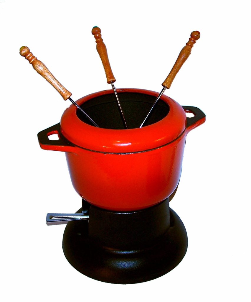 A red enameled fondue pot on a black burner stand with three wooden-handled fondue forks