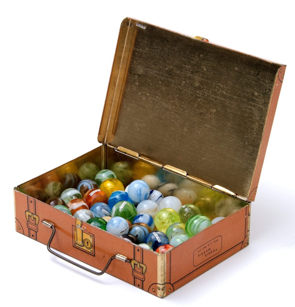 An open tin box printed to look like a little brown suitcase, filled with swirled glass marbles in blue, green, yellow and white