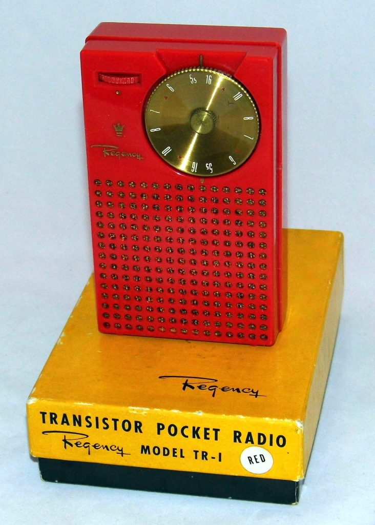 A red Regency TR-1 pocket radio with a gold tuning dial and dotted speaker grille, standing on its yellow box labeled Transistor Pocket Radio, Regency Model TR-1