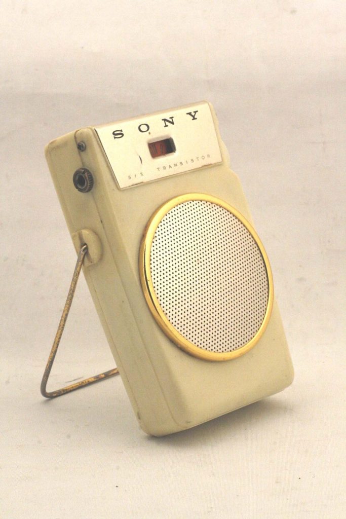 A cream-colored Sony six-transistor pocket radio with a round gold-rimmed speaker grille, propped on a wire stand