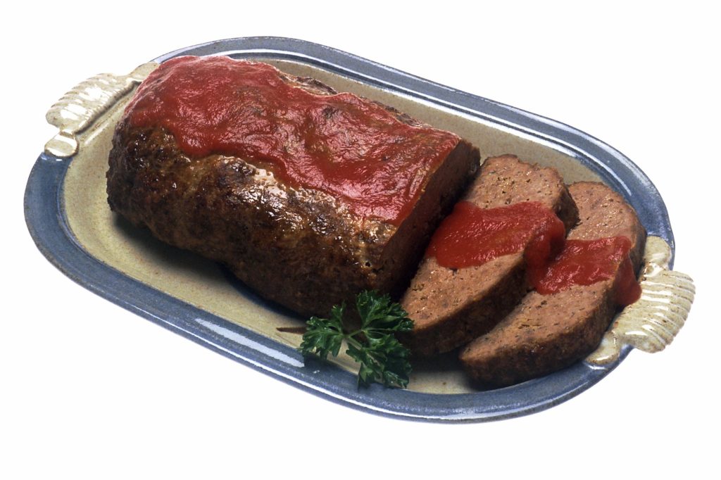 A meatloaf glazed with red tomato sauce on an oval platter, with two slices cut and a sprig of parsley.