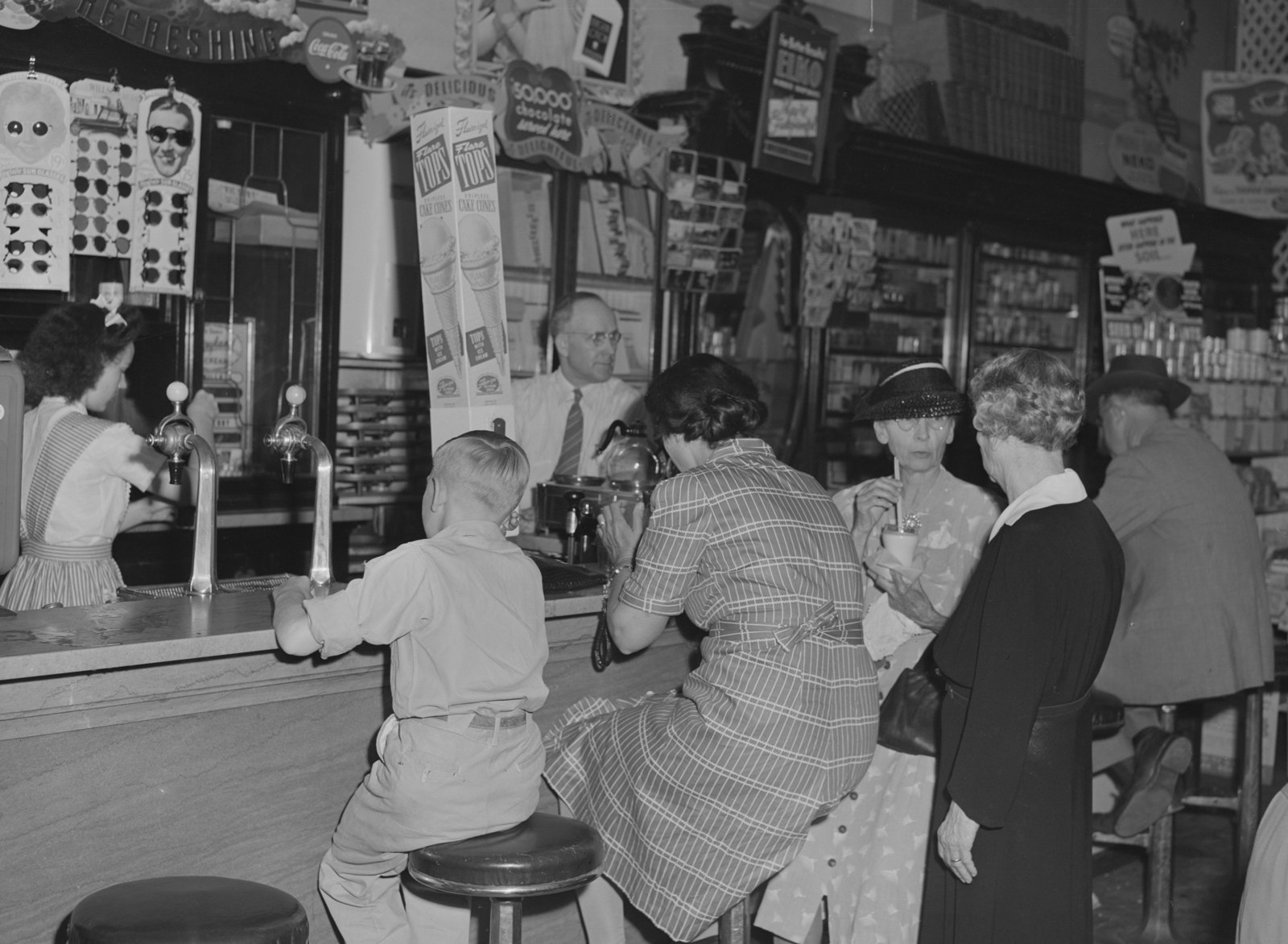 Customers, including a boy, sit on stools at a drugstore soda fountain while a soda jerk works behind the counter.